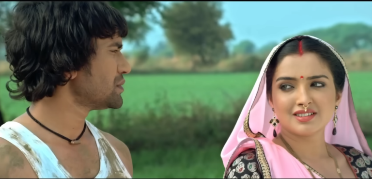 A man with a rugged appearance, wearing a sleeveless vest and a black necklace, standing in an outdoor rural setting.