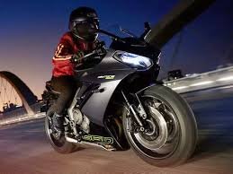 Rider on a Triumph Daytona 660 sport bike speeding on a highway at night, wearing a red jacket and black helmet