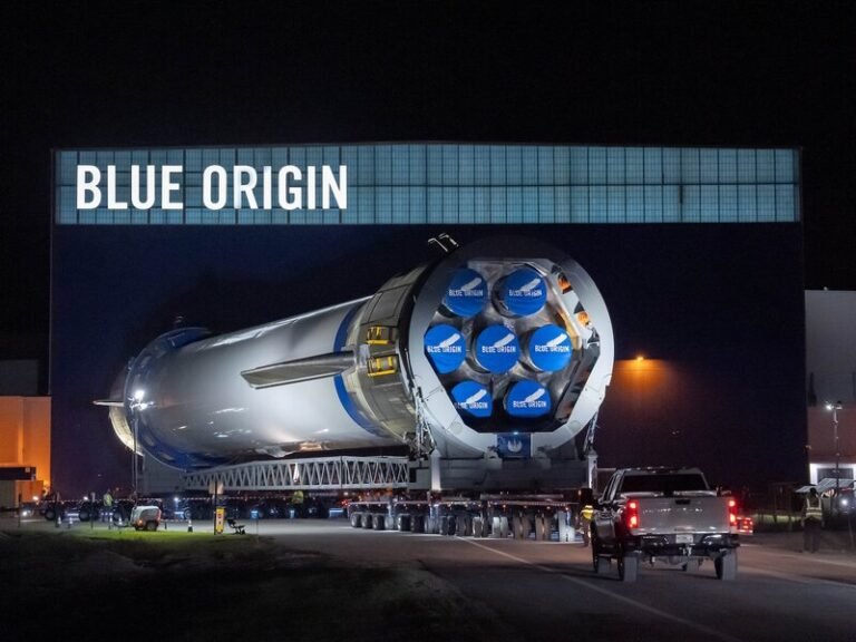 Breaking News Visual Prompt: Create a high-resolution news-style image showcasing Blue Origin’s New Glenn rocket being rolled out at night from its hangar in Cape Canaveral Space Force Station. The rocket should appear massive and futuristic under floodlights, with “BLUE ORIGIN” branding clearly visible on the building. Include subtle reflections on the metal body and a convoy of support vehicles nearby for scale. The atmosphere should feel anticipatory and historic, symbolizing the company’s upcoming Mars mission with NASA’s ESCAPADE probes. Theme: Space exploration, innovation, private spaceflight, Mars mission Style: Realistic photojournalism — dramatic lighting, cinematic night scene, suitable for front-page feature or Google Discover thumbnail. Text overlay suggestion (optional): “Blue Origin’s New Glenn Ready for Mars Mission” Aspect Ratio: 16:9 Resolution: 600 × 800 (news-optimized for mobile and web) Focus Keyword: Blue Origin Mars Mission